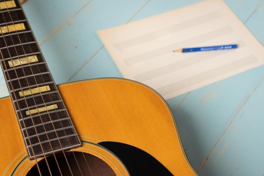 Music recording scene with guitar, empty music sheet and pencil on wooden table