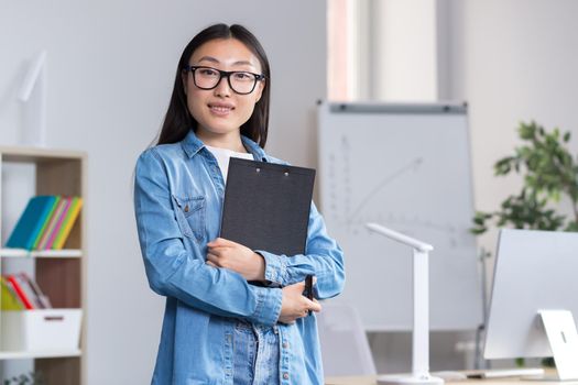 Young beautiful Asian female teacher looking at the camera and smiling, portrait of a woman in the office.