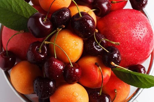 apricots and cherries in a metal bowl on a white background. Close-up