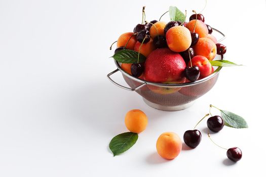 apricots and cherries in a metal bowl on a white background. Copy spase