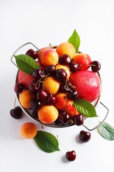 apricots and cherries in a metal bowl on a white background. Top view