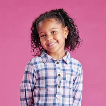 A portrait of a pretty little mixed race girl with curly hair posing against a pink copyspace background in a studio. A smiling African child wearing casual clothes indoors.