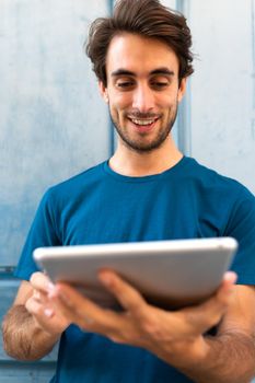 Vertical portrait of happy smiling young caucasian man using digital tablet outdoors. Selective focus on face. Wireless technology and social media concept.