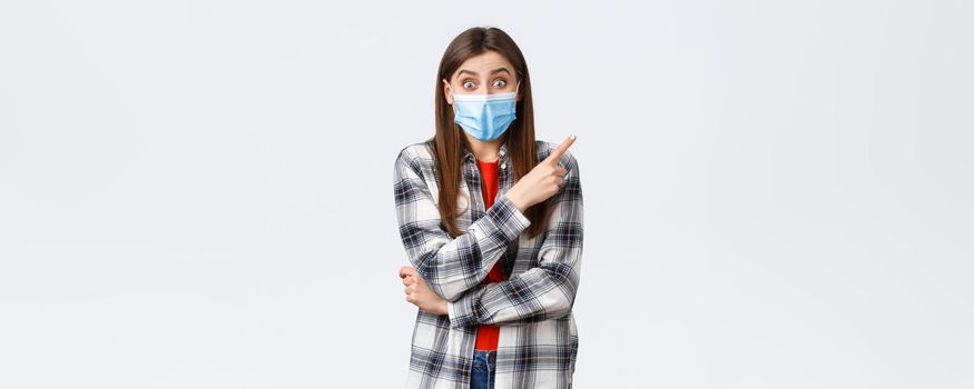 Coronavirus outbreak, leisure on quarantine, social distancing and emotions concept. Excited and rejoicing young girl in medical mask, pointing finger upper right corner at amazing promo.