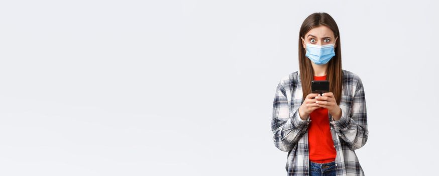 Different emotions, covid-19, social distancing and technology concept. Puzzled and confused young woman in medical mask react to strange message, hold mobile phone, look camera unsure.