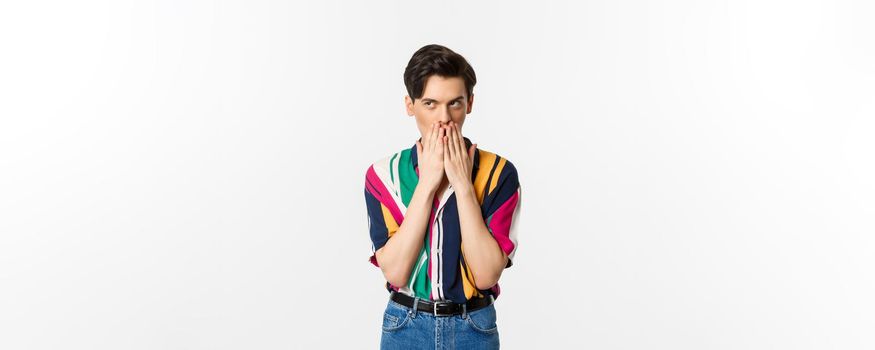 Image of cunning young man looking at upper left corner, scheming something, standing over white background.