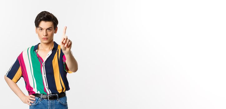 Disappointed young man prohibit something, shaking finger in disapproval, forbid you, standing over white background.