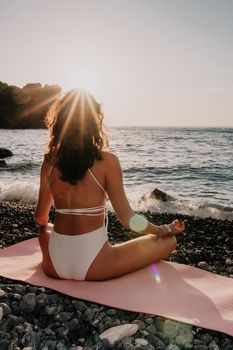 Young woman in swimsuit with long hair practicing stretching outdoors on yoga mat by the sea on a sunny day. Women's yoga fitness pilates routine. Healthy lifestyle, harmony and meditation concept.