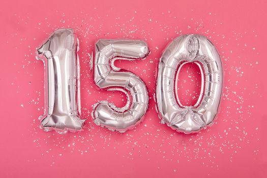 Silver balloon number 150 one hundred fifty shape sparkles scattered randomly on juicy pink background. Silver confetti pink background