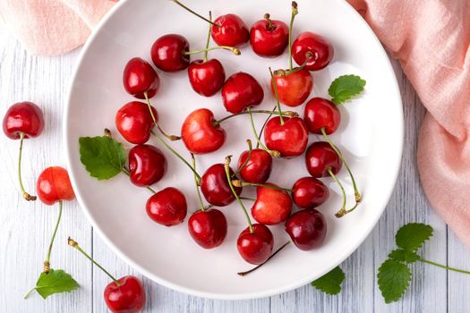 Ripe juicy sweet cherry lies on a white porcelain plate on a light wooden surface. Summer healthy food. Selective focus. View from above.