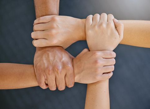 Closeup of diverse group of people from above holding each others wrists in a circle to express unity, support and solidarity. Connected hands of multiracial community linked for teamwork in a huddle. Society join together for collaboration and equality.