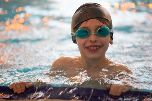 Boy in a swimming cap and swimming goggles in the pool. The child is engaged in the swimming section.