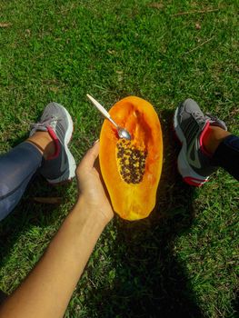 girl sits on a lawn and holds a half of delicious papaya with a spoon. download photo