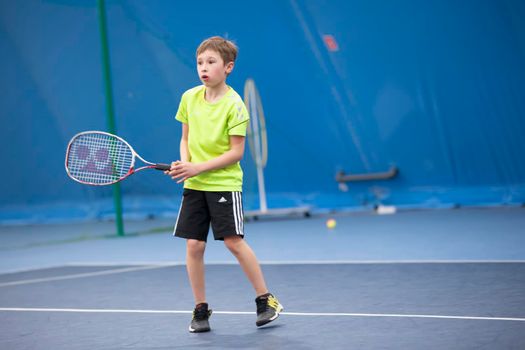 A boy with a tennis racket on the court plays tennis.