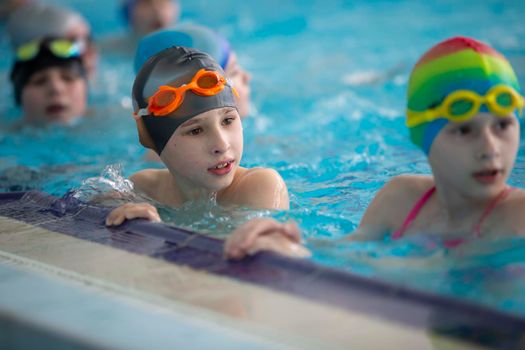 Boy in a swimming cap and swimming goggles in the pool. The child is engaged in the swimming section.