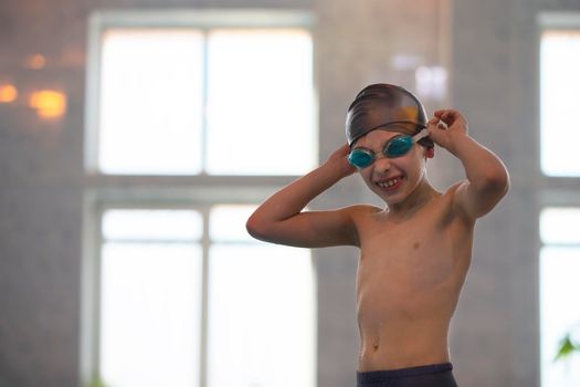 Boy in a swimming cap and swimming goggles in the pool. The child is engaged in the swimming section.