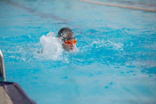 A boy in a swimming cap and glasses is swimming in the sports pool.