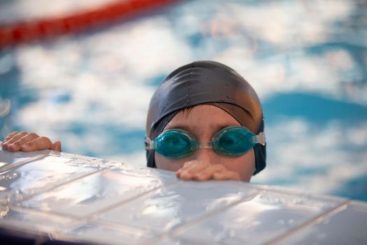 Boy in a swimming cap and swimming goggles in the pool. The child is engaged in the swimming section.