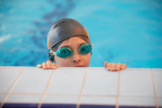 Boy in a swimming cap and swimming goggles in the pool. The child is engaged in the swimming section.