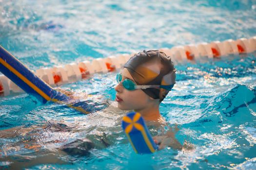 Boy in a swimming cap and swimming goggles in the pool. The child is engaged in the swimming section.