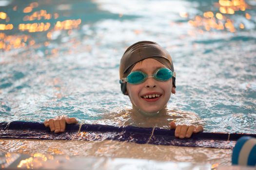 Boy in a swimming cap and swimming goggles in the pool. The child is engaged in the swimming section.