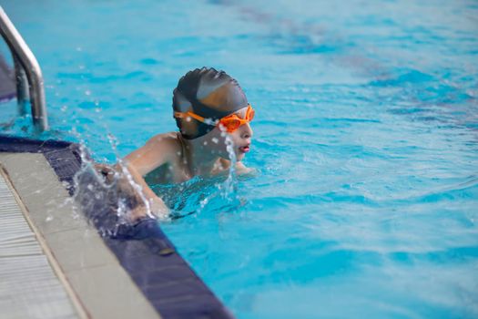 A boy in a swimming cap and glasses is swimming in the sports pool.