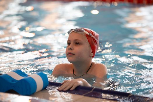 Boy in a swimming cap and swimming goggles in the pool. The child is engaged in the swimming section.