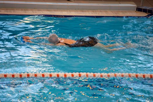 A woman swims in a black swimsuit and a swimming cap swims in the pool.