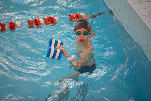 Boy in a swimming cap and swimming goggles in the pool. The child is engaged in the swimming section.