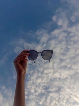 woman hand with sunglasses on background of blue sky. look on the sky through sunglasses. download photo