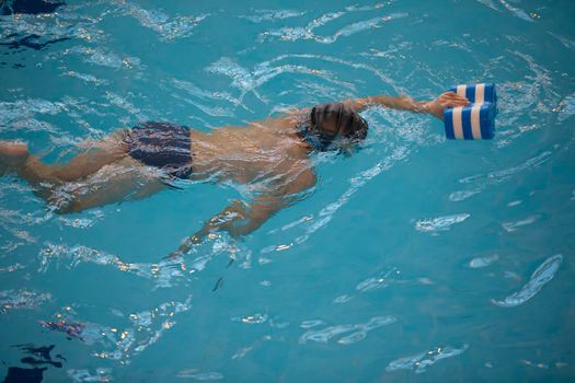 Boy in a swimming cap and swimming goggles in the pool. The child is engaged in the swimming section.