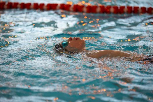 Boy in a swimming cap and swimming goggles in the pool. The child is engaged in the swimming section.