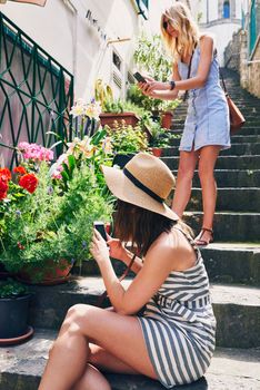 Two friends taking photos of pot flowers using smartphone for social media while on adventure travel vacation.