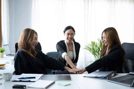 Group of businesswomen stacking hands together for showing unity support at office.