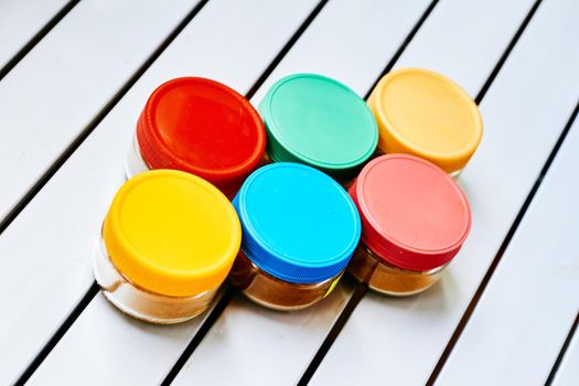 an aromatic or pungent vegetable substance used to flavor food, e.g. cloves, pepper, or cumin. spice storage containers. containers on a white striped table.