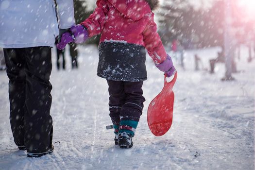 The girl is holding a red sled in her hands to ride the hill. Sledging. Activities for children and teenagers. Winter entertainment and sports