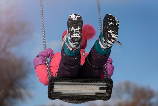 Happy girl on a swing in winter. A small child plays on the winter playground. Fun for kids in winter outdoors.