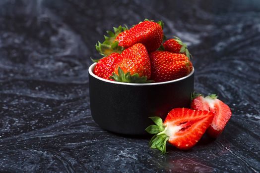 Strawberries on black marble. Ripe strawberries in a saucer on a black background. Place to insert text.