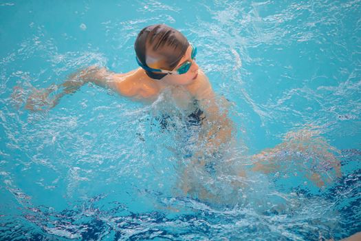 Boy in a swimming cap and swimming goggles in the pool. The child is engaged in the swimming section.