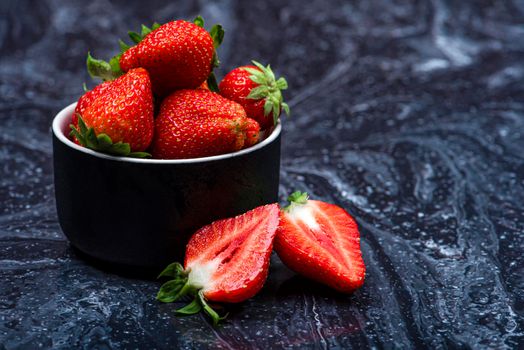 Strawberries on black marble. Ripe strawberries in a saucer on a black background. Place to insert text.