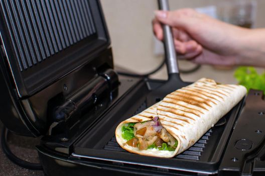 Roll of pita bread, vegetables and chicken. Cooking on an electric grill. Kebab, shawarma