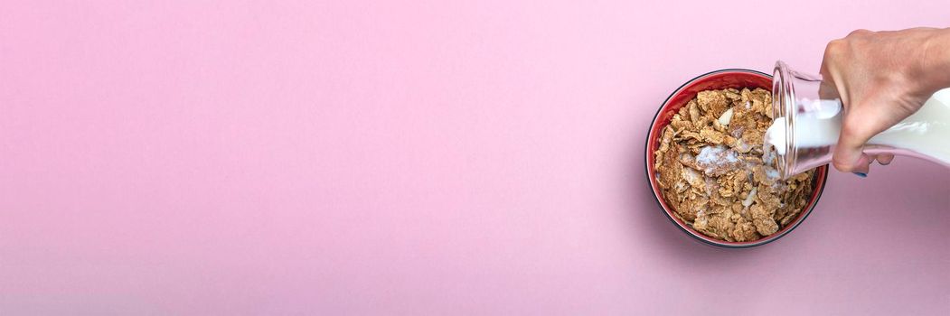 Cooking muesli. A woman pours milk from a jug into a saucer with muesli flakes. Pink background with place to insert text. Large banner for print or advertising.