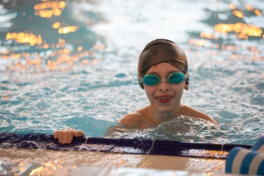 Boy in a swimming cap and swimming goggles in the pool. The child is engaged in the swimming section.