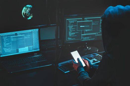 Overhead hacker in hood working at laptop and mobile phone typing text in dark room, An anonymous hacker uses malware with mobile phone to hack password, personal data steals money from bank. cyber. Download photo