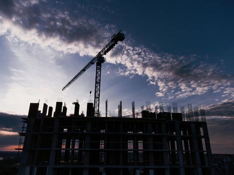 Tower crane and building construction site silhouette at sunrise. The construction crane and the building against the blue sky. download photo