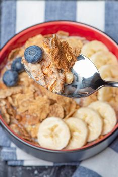 Muesli. Breakfast, healthy food and diet. Muesli with milk and fruit in a plate on a black marble top. Woman's hand with a spoon.