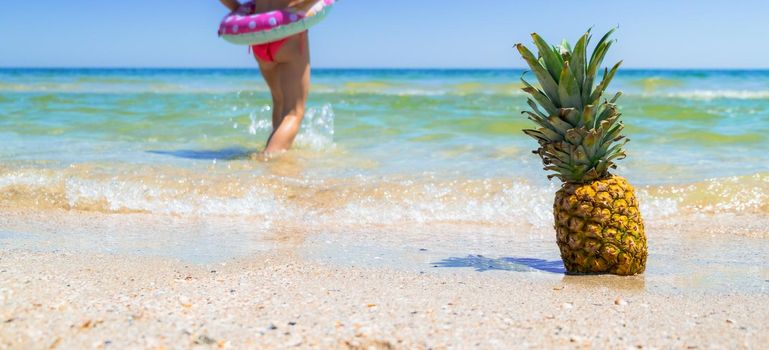 Pineapple on the beach with child going in water sea. Pineapple fruit in the sea waves. Leisure in summer and Summer vacation concept. . High quality photo