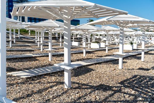 Rows of wooden umbrellas from the sun on the seashore in the morning. Wooden paths on the sand between umbrellas. Beach holiday at the resort