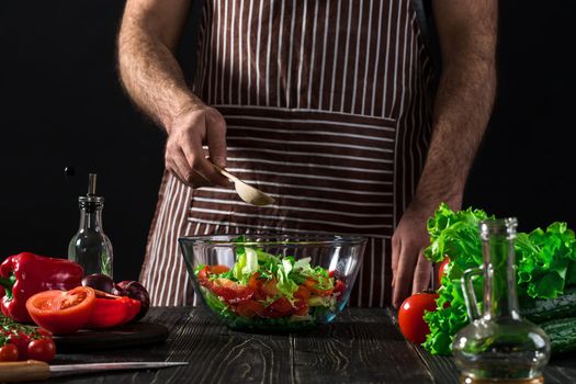 Man preparing salad with fresh vegetables on a wooden table. Cooking tasty and healthy food. On black background. Vegetarian food, healthy or cooking concept.