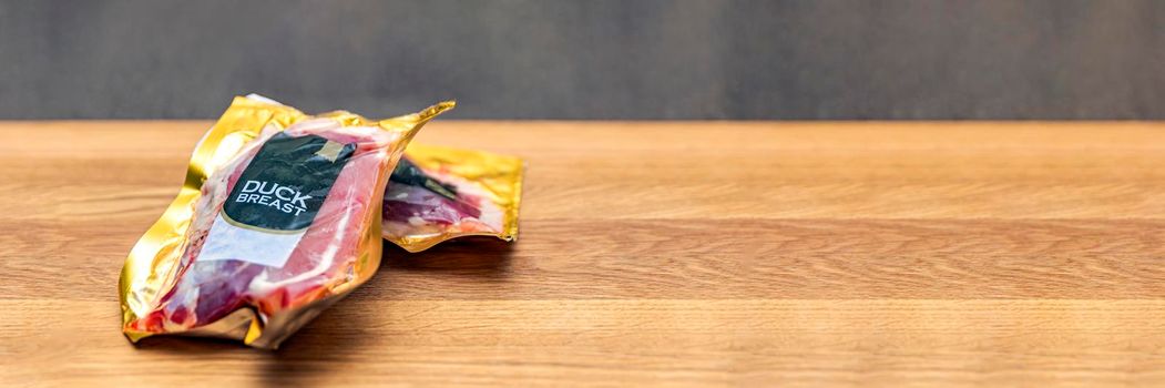 Vacuum packed duck breast. Duck meat in vacuum plastic packaging on a wooden cutting board, background for a culinary theme, place for text. Copy space